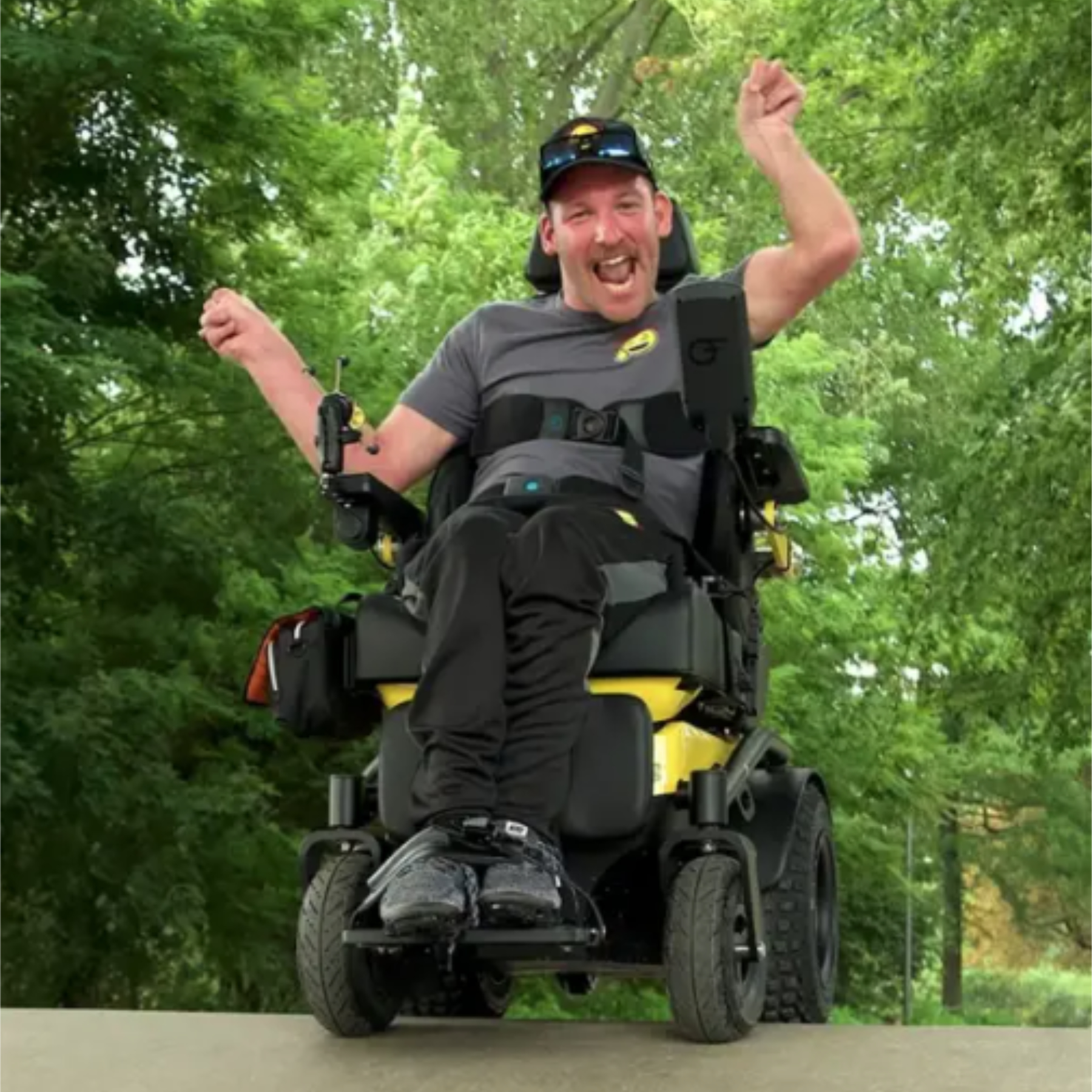 Man cheering with arms raised in a yellow Freedom One Life Series 5 powerchair outdoors