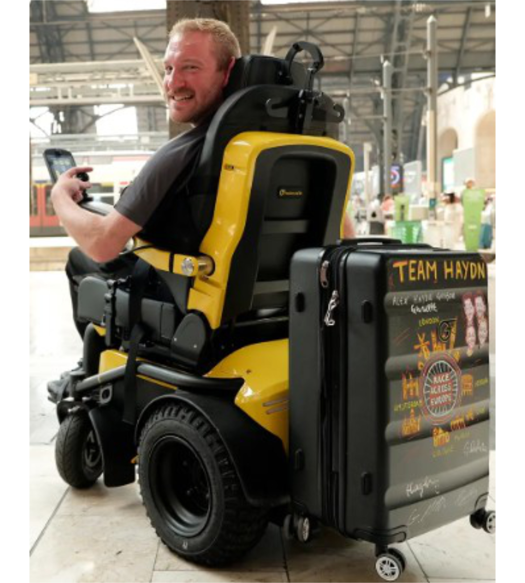 Man in a yellow Series 5 powerchair with a suitcase at a station